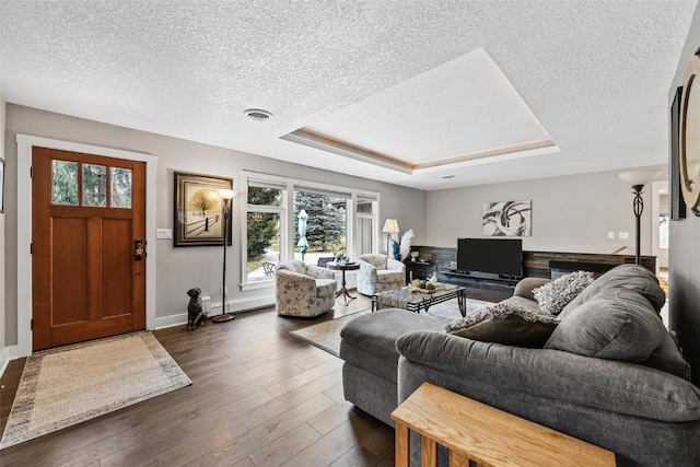 living room with dark hardwood / wood-style flooring, a wealth of natural light, a raised ceiling, and a textured ceiling