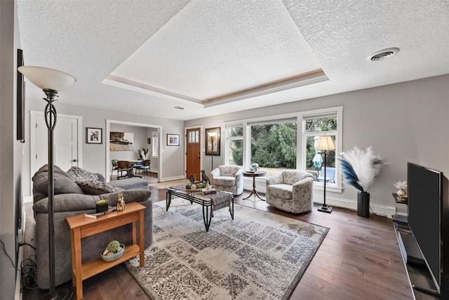 living room featuring dark hardwood / wood-style floors, a textured ceiling, and a tray ceiling