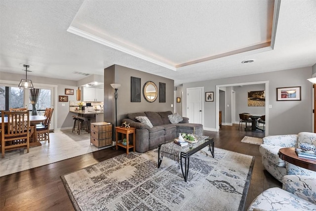 living room featuring dark wood-type flooring, a tray ceiling, and a textured ceiling