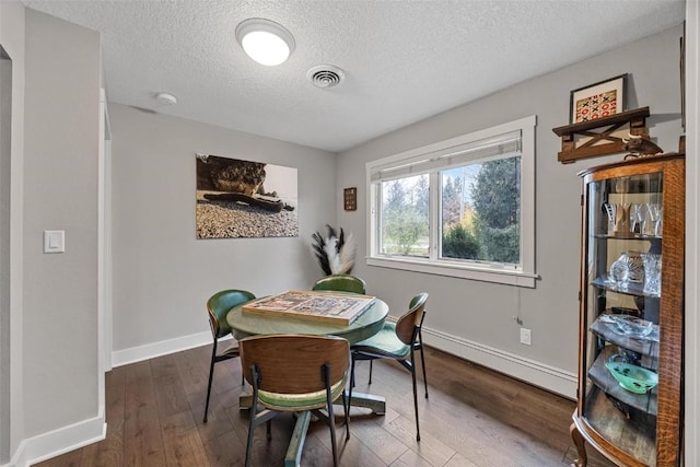 dining area with baseboard heating, hardwood / wood-style floors, and a textured ceiling