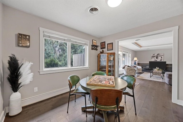 dining area with baseboard heating, hardwood / wood-style floors, and a textured ceiling