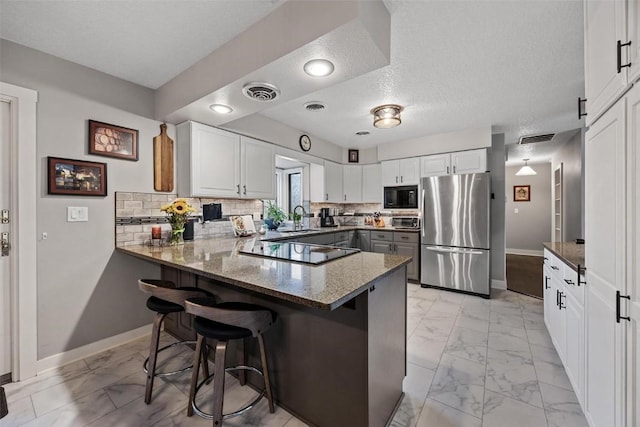 kitchen with black appliances, kitchen peninsula, white cabinets, and a kitchen bar