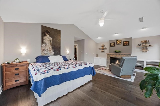 bedroom featuring dark hardwood / wood-style flooring, a tiled fireplace, vaulted ceiling, and ceiling fan