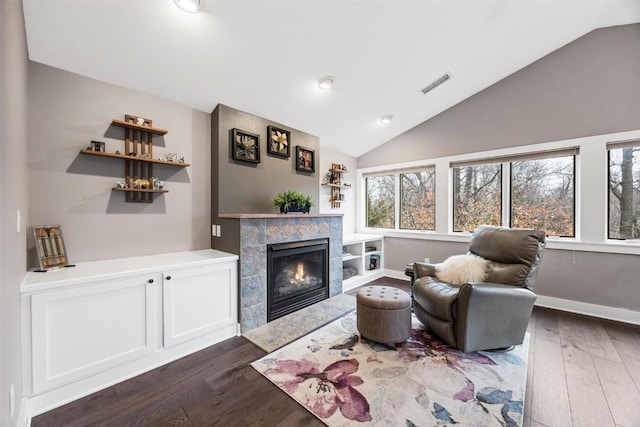 living room featuring lofted ceiling, dark hardwood / wood-style flooring, and a tiled fireplace