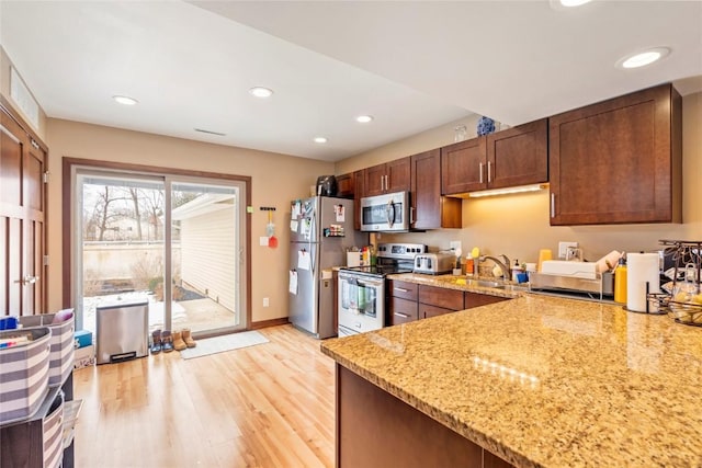 kitchen with appliances with stainless steel finishes, kitchen peninsula, sink, light hardwood / wood-style floors, and light stone counters