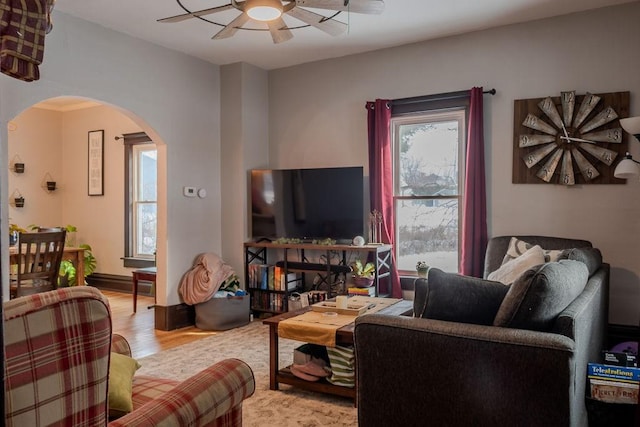 living area with arched walkways, ceiling fan, and wood finished floors