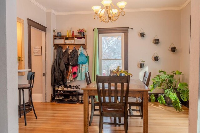 dining space with light wood-style flooring, crown molding, and an inviting chandelier