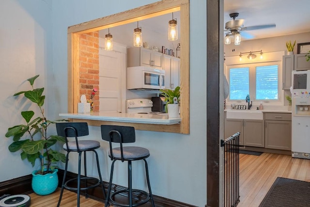 kitchen with a sink, a kitchen breakfast bar, white appliances, light wood-style floors, and ceiling fan