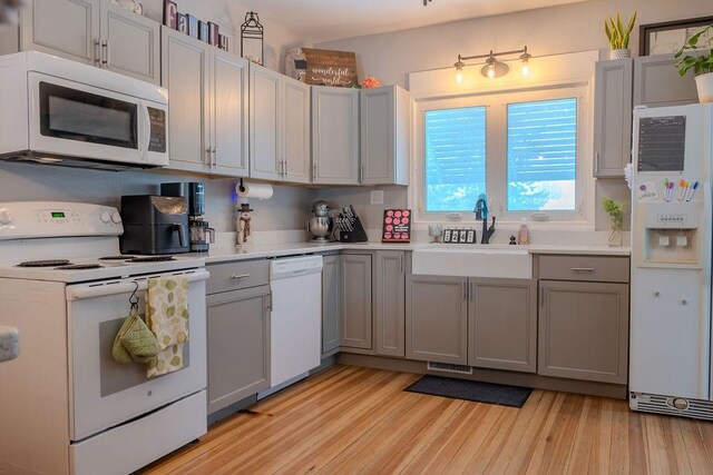 kitchen with gray cabinets, sink, white appliances, and light wood-type flooring