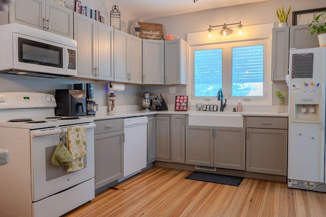 kitchen with a sink, white appliances, gray cabinets, and light countertops