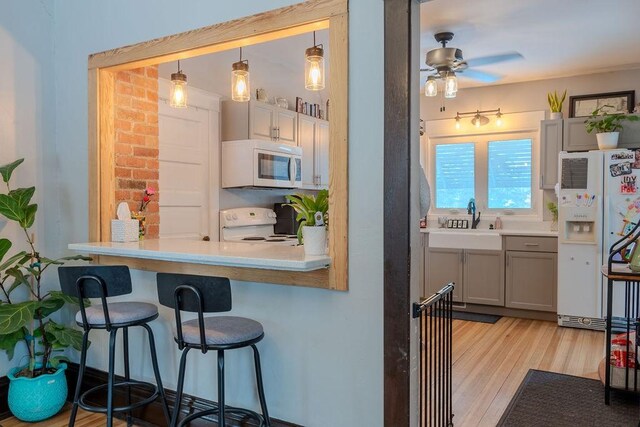 kitchen with a breakfast bar area, gray cabinetry, light hardwood / wood-style flooring, hanging light fixtures, and white appliances