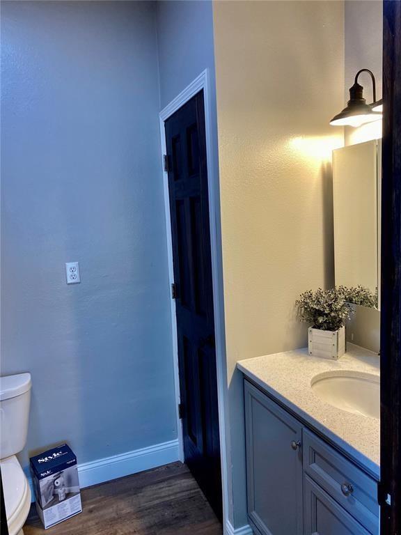 bathroom with toilet, vanity, baseboards, and wood finished floors