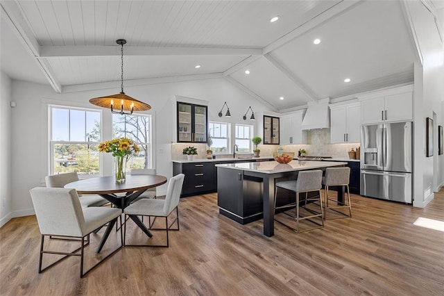 kitchen with stainless steel refrigerator with ice dispenser, hanging light fixtures, custom range hood, a kitchen island, and decorative backsplash