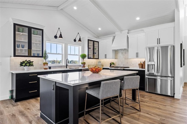 kitchen featuring appliances with stainless steel finishes, lofted ceiling with beams, custom exhaust hood, a center island, and light wood-type flooring