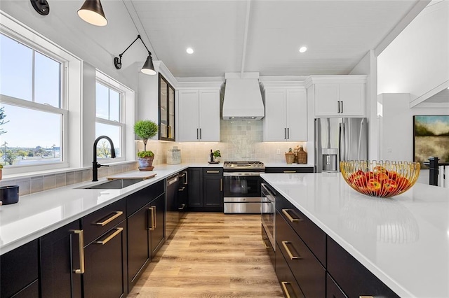 kitchen with sink, white cabinetry, appliances with stainless steel finishes, custom range hood, and backsplash