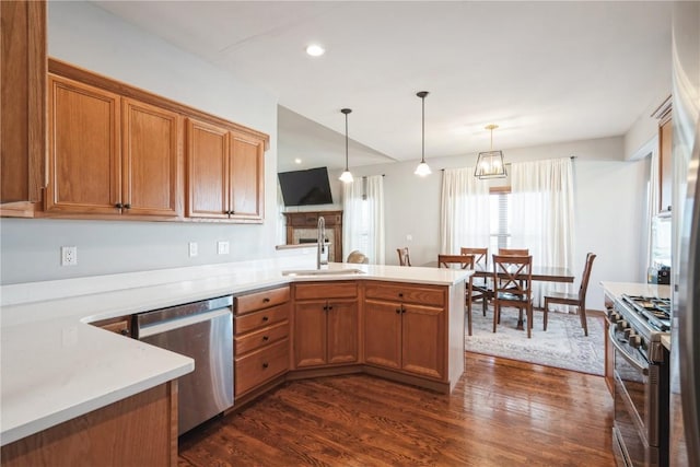 kitchen with appliances with stainless steel finishes, decorative light fixtures, sink, kitchen peninsula, and dark wood-type flooring