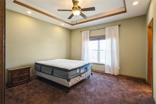 bedroom featuring ceiling fan, a tray ceiling, and dark carpet