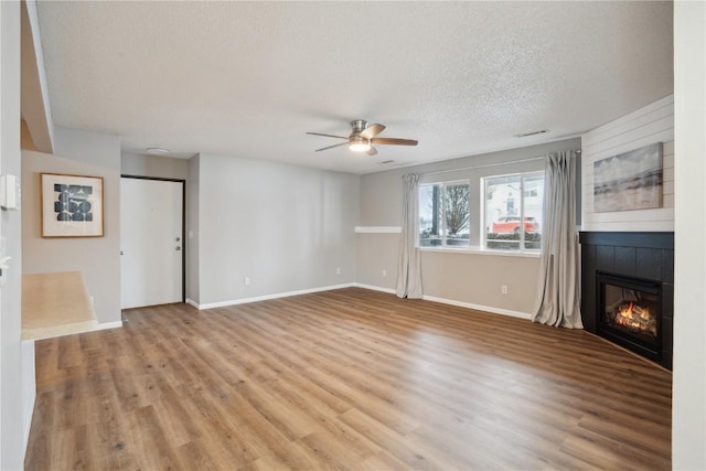 unfurnished living room featuring ceiling fan, a fireplace, light hardwood / wood-style floors, and a textured ceiling