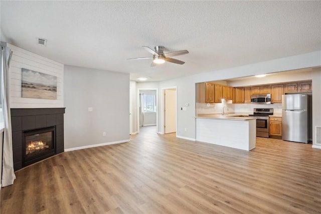 kitchen with a tiled fireplace, kitchen peninsula, stainless steel appliances, a textured ceiling, and light wood-type flooring