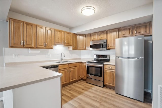 kitchen featuring sink, kitchen peninsula, stainless steel appliances, a textured ceiling, and light hardwood / wood-style flooring