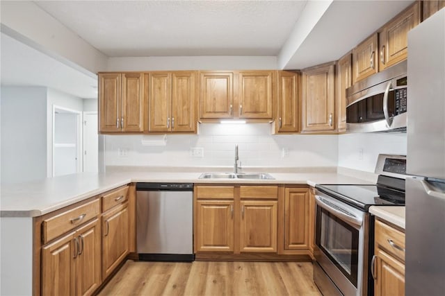 kitchen featuring stainless steel appliances, sink, light hardwood / wood-style flooring, and kitchen peninsula