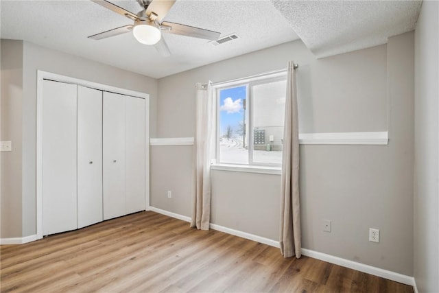 unfurnished bedroom featuring a textured ceiling, light hardwood / wood-style flooring, a closet, and ceiling fan