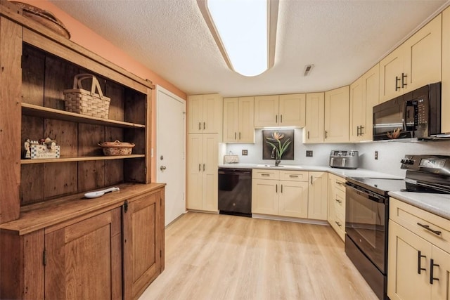 kitchen featuring sink, a textured ceiling, light hardwood / wood-style flooring, cream cabinets, and black appliances