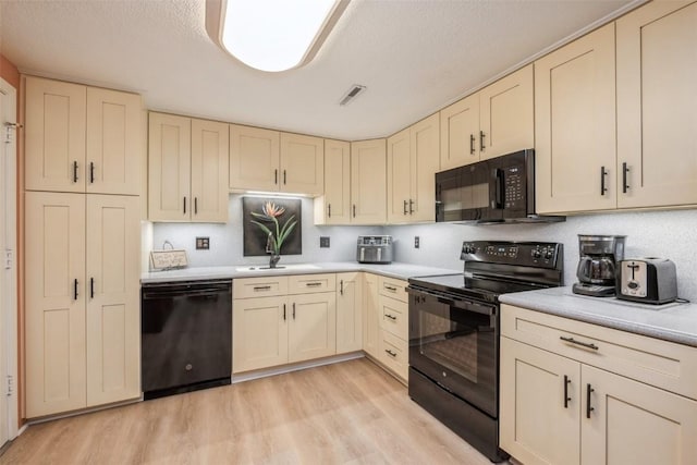 kitchen with cream cabinets, sink, light hardwood / wood-style floors, and black appliances