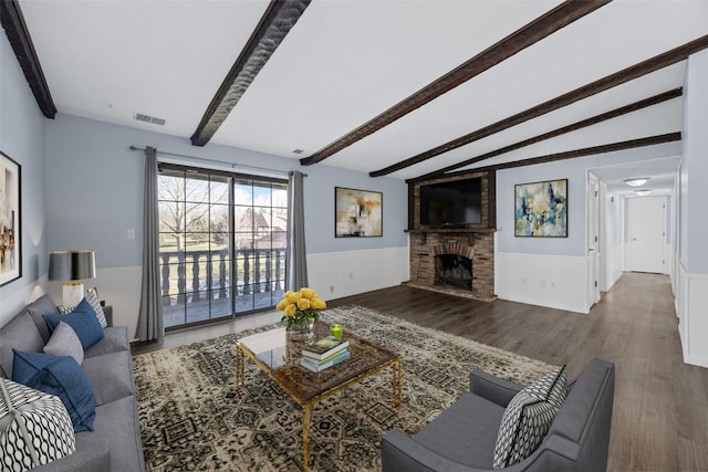 living room with hardwood / wood-style flooring, a stone fireplace, and lofted ceiling with beams