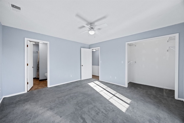 unfurnished bedroom featuring ceiling fan, dark carpet, a closet, and a walk in closet