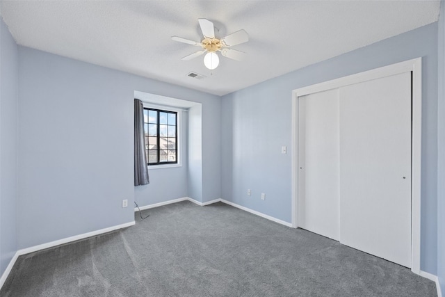 unfurnished bedroom with ceiling fan, dark carpet, and a closet