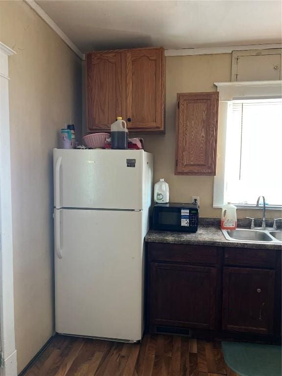 kitchen with dark countertops, brown cabinetry, freestanding refrigerator, a sink, and black microwave