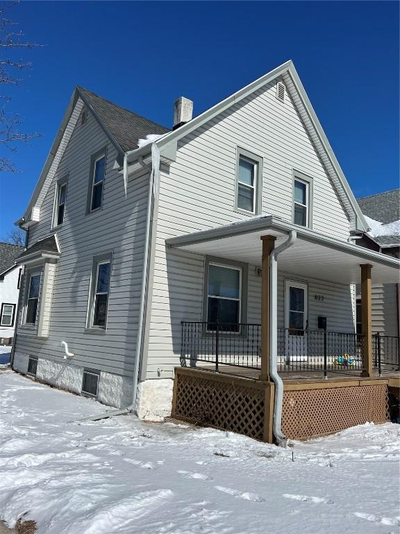 snow covered house with a porch and a chimney