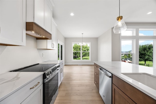 750 Hampshire Dr, Marion, IA 52302 - kitchen featuring appliances with stainless steel finishes, extractor fan, light wood finished floors, hanging light fixtures, and white cabinets