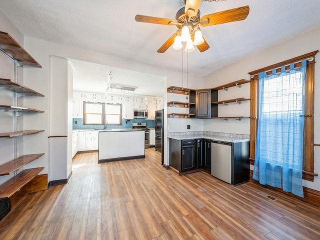 kitchen with open shelves, light countertops, appliances with stainless steel finishes, a sink, and light wood-type flooring