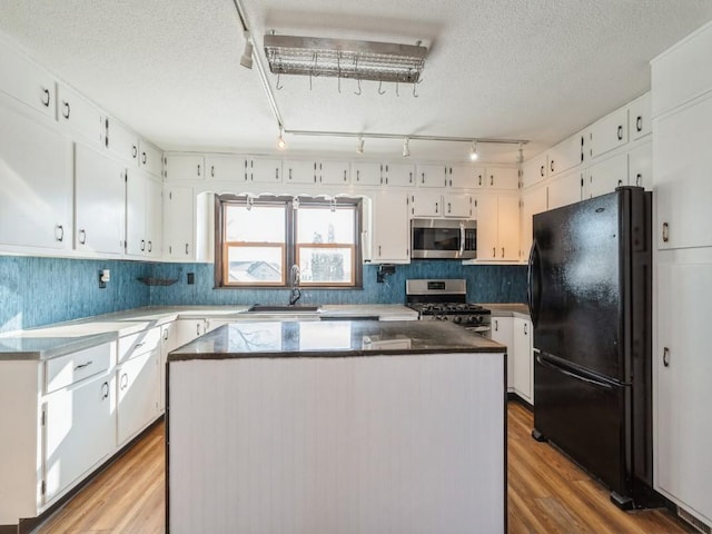 kitchen with stainless steel appliances, white cabinetry, a sink, and wood finished floors