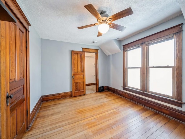 additional living space featuring a textured ceiling, ceiling fan, light wood-type flooring, and baseboards