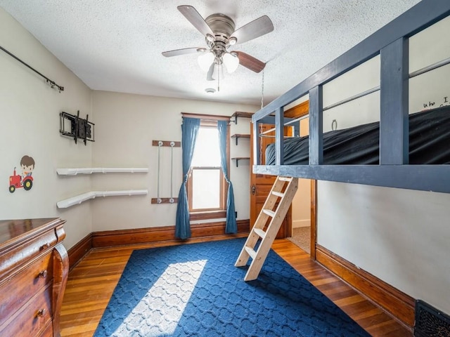 unfurnished bedroom with a ceiling fan, a textured ceiling, baseboards, and wood finished floors