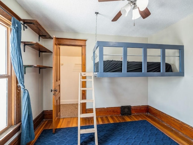 unfurnished bedroom featuring ceiling fan, a textured ceiling, baseboards, and wood finished floors