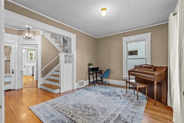 miscellaneous room with crown molding, an inviting chandelier, a textured ceiling, and light wood-type flooring