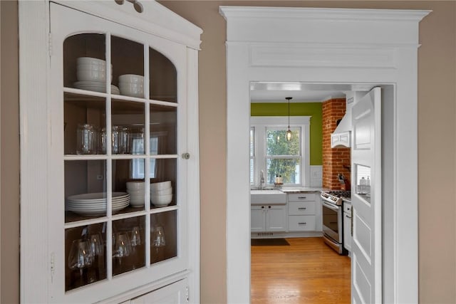 kitchen featuring white cabinets, custom exhaust hood, hanging light fixtures, gas stove, and light wood-type flooring