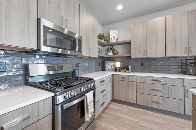 kitchen with lofted ceiling, light brown cabinetry, tasteful backsplash, light wood-type flooring, and appliances with stainless steel finishes