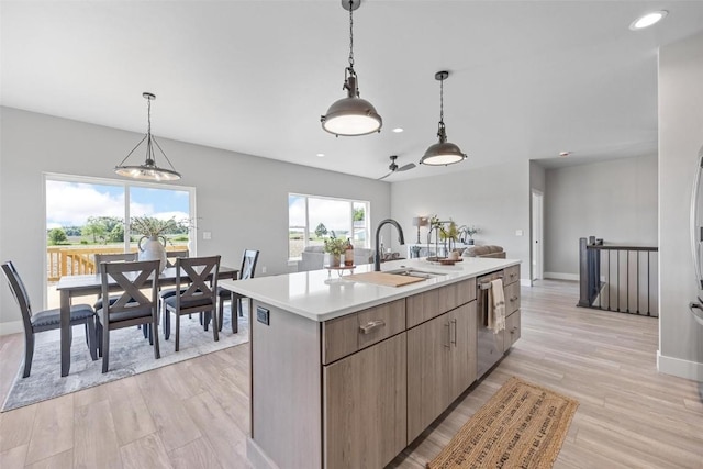 kitchen featuring pendant lighting, sink, light hardwood / wood-style flooring, dishwasher, and an island with sink