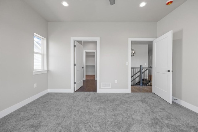 unfurnished bedroom featuring a spacious closet, dark carpet, and a closet