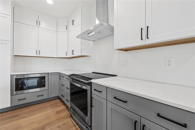 kitchen featuring black microwave, gray cabinetry, white cabinets, wall chimney range hood, and electric stove