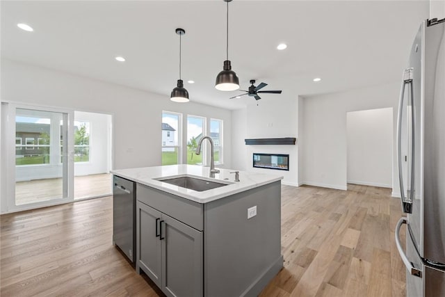 kitchen with sink, gray cabinetry, a kitchen island with sink, stainless steel appliances, and light hardwood / wood-style flooring