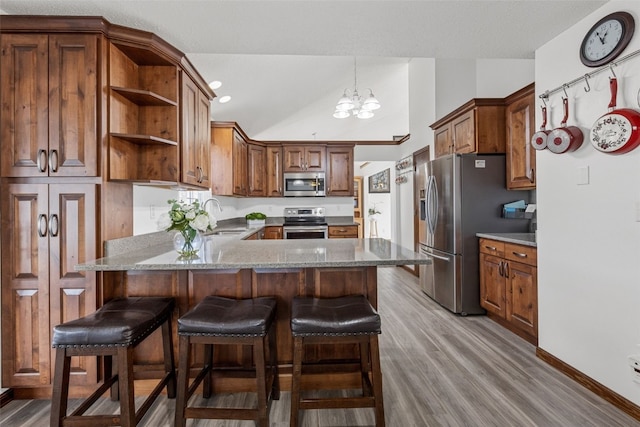 kitchen featuring appliances with stainless steel finishes, lofted ceiling, sink, an inviting chandelier, and light hardwood / wood-style flooring