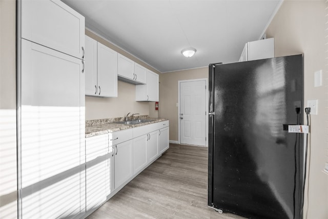 kitchen featuring black refrigerator, sink, and white cabinets