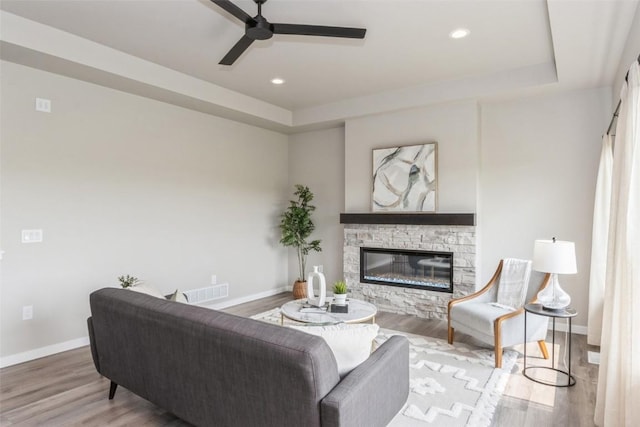 living room featuring ceiling fan, a tray ceiling, a fireplace, and wood-type flooring