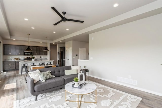 living room featuring ceiling fan, light hardwood / wood-style floors, and a tray ceiling